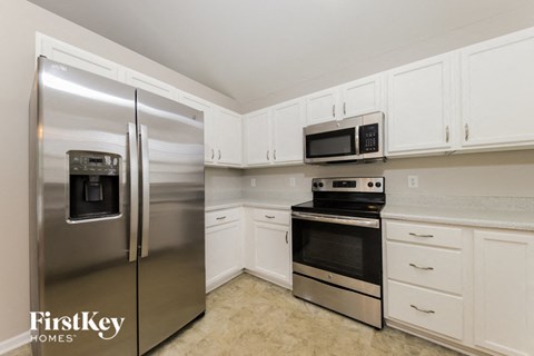 A kitchen with a stainless steel refrigerator, microwave, oven, and white cabinets.