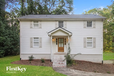 the front of a white house with a lawn and trees