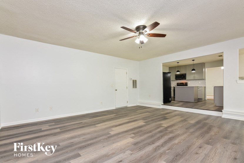 an empty living room with a ceiling fan and a kitchen