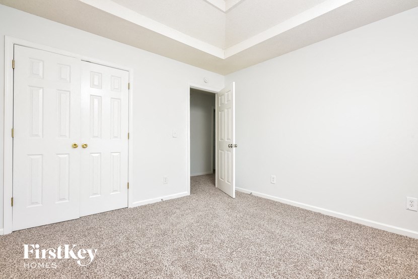 a bedroom with white walls and carpet and a door to a closet