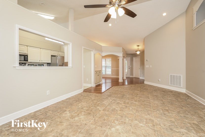 A spacious room with a fan and a kitchen area in the background.