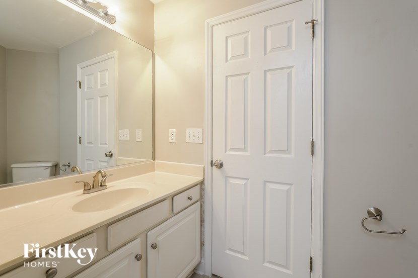 A white bathroom with a sink, mirror, and door.