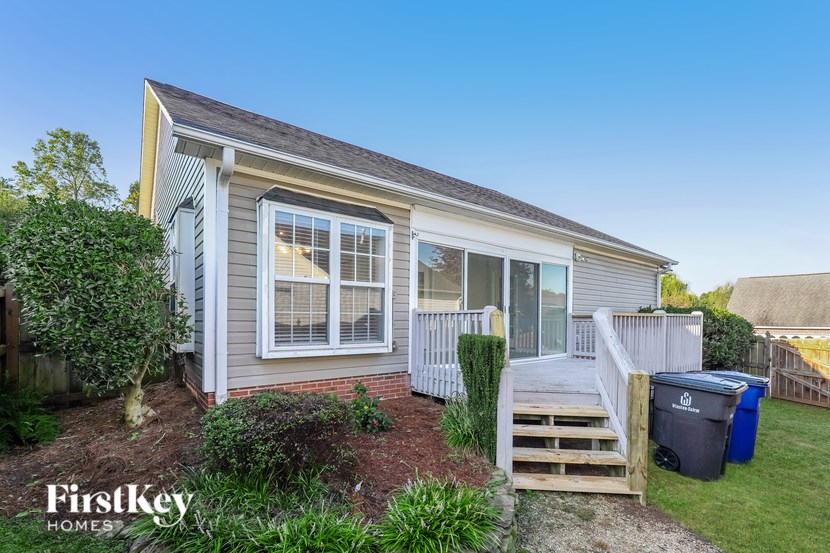 A small house with a porch and a trash can in front.