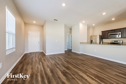 A spacious room with wooden flooring and a kitchen area in the background.