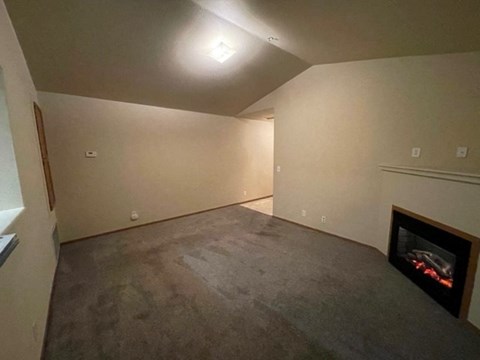 A living room with a fireplace and a grey carpet.