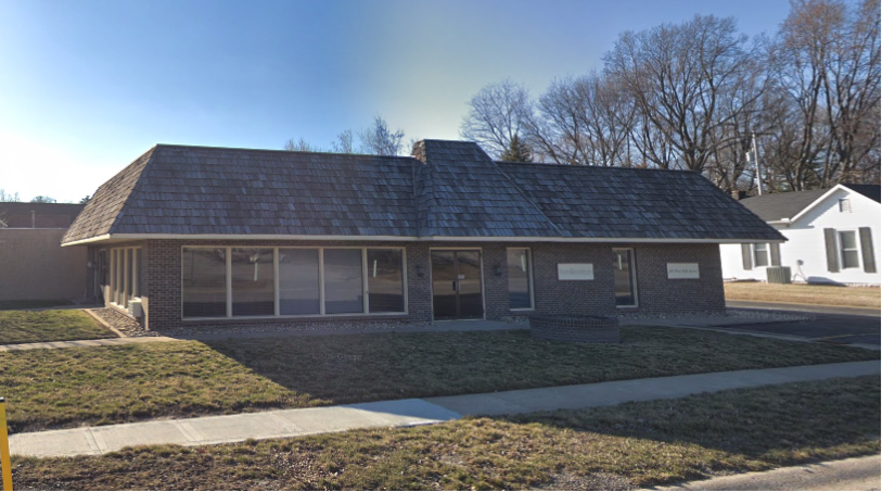 the front of a brick house with a lawn and a sidewalk