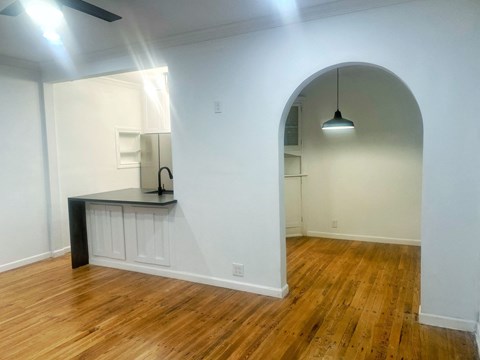 an arched opening into a living room with wood flooring and a kitchen