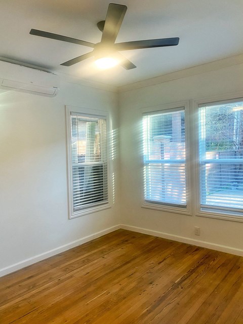 an empty bedroom with a ceiling fan and three windows
