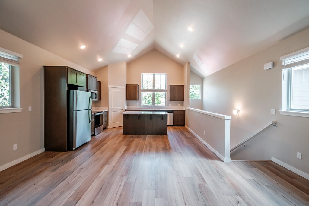 an empty kitchen with wooden floors and a black refrigerator