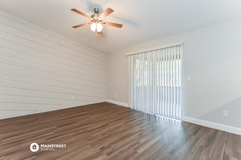 the living room of an apartment with wood flooring and a ceiling fan