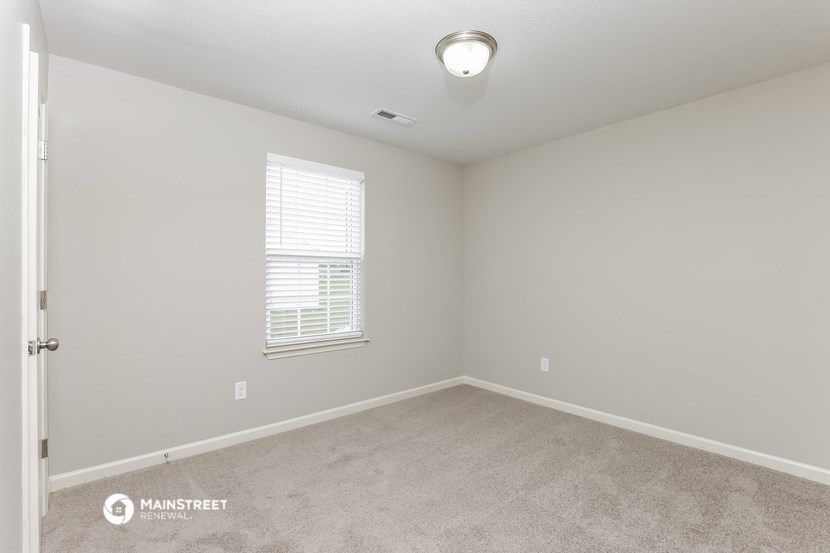the spacious bedroom with carpeted flooring and a window