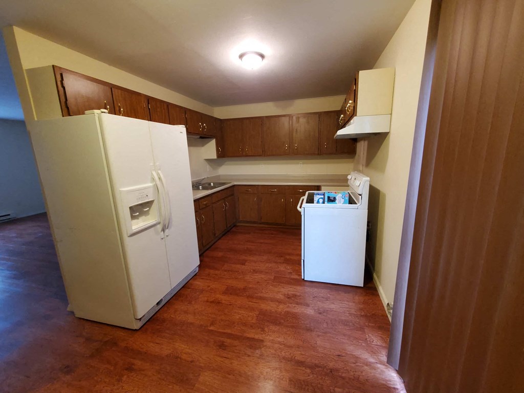 A kitchen with a white fridge and wooden floors.