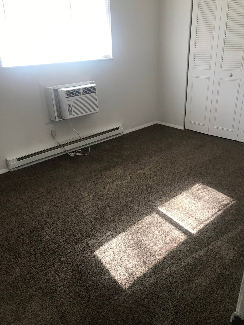 A room with a window, a carpet, and a wall-mounted air conditioner unit.