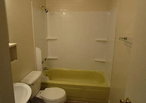A white toilet sits next to a yellow bathtub in a small bathroom.