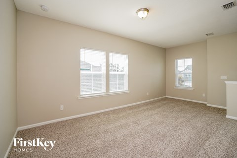 a spacious living room with carpet and two windows