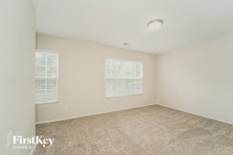 a spacious living room with carpet and two windows