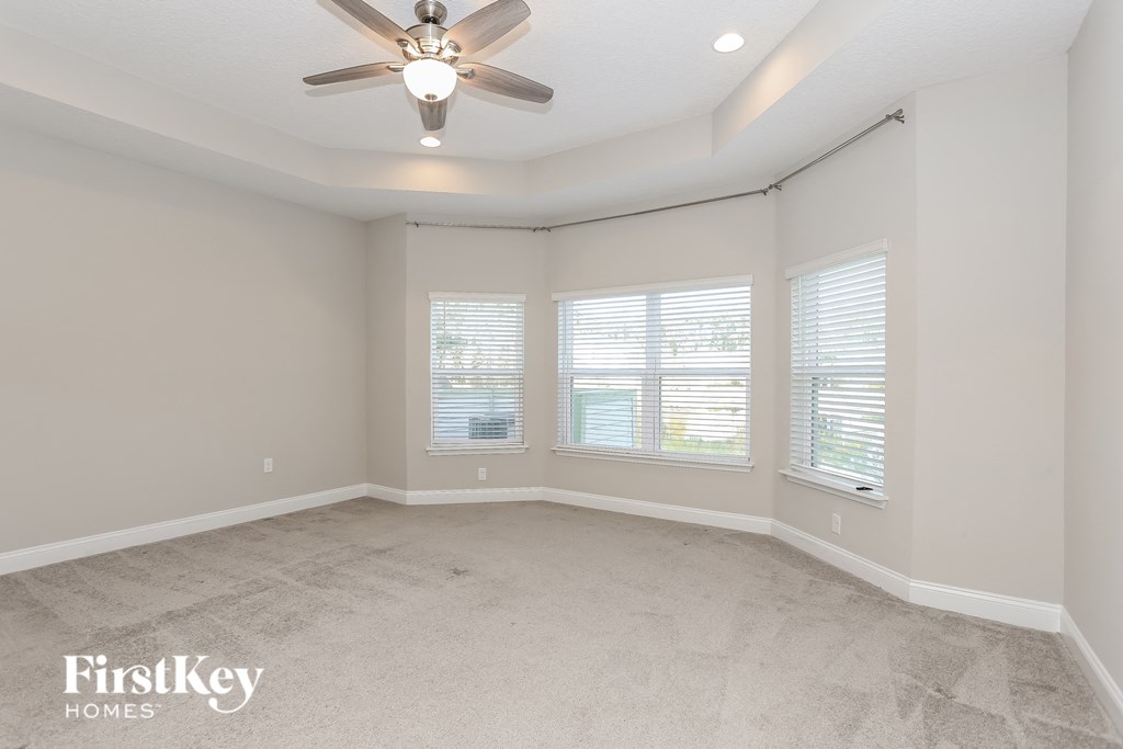 an empty living room with a ceiling fan and three windows