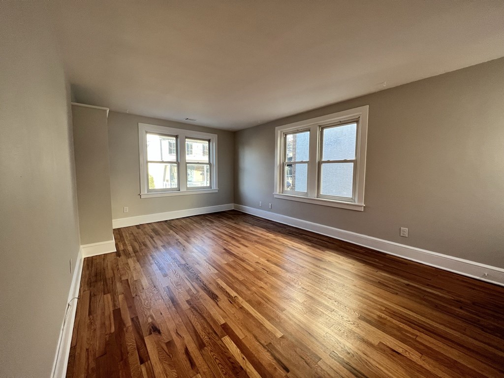 an empty living room with hard wood floors and two windows
