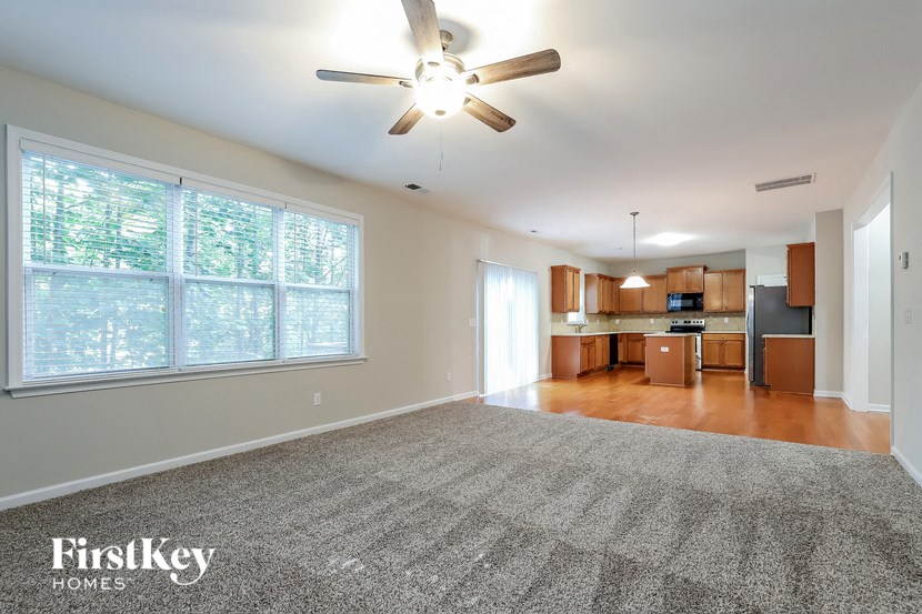 an empty living room with a ceiling fan and a kitchen