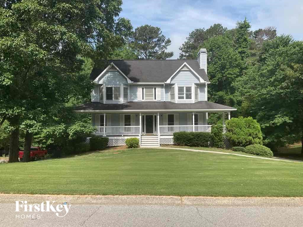 A white house with a black roof and a chimney is surrounded by greenery.