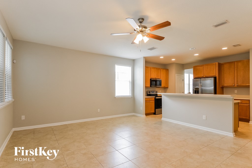an empty living room with a kitchen and a ceiling fan