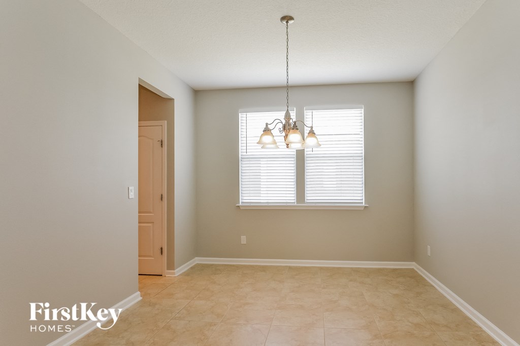 an empty dining room with a window and a chandelier