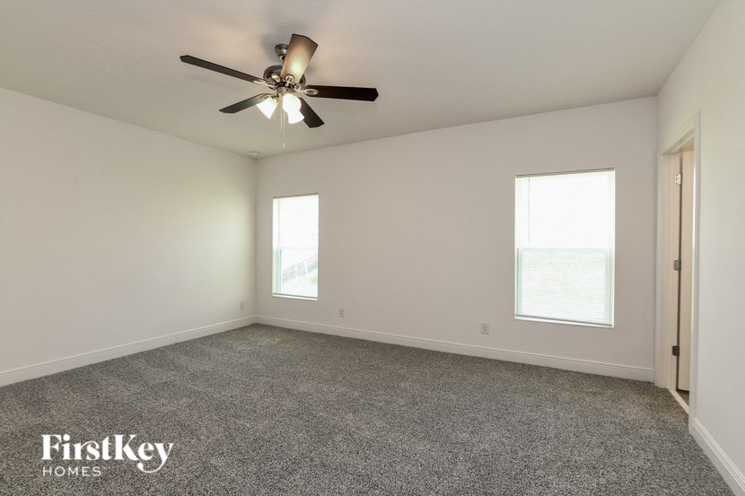 an empty living room with a ceiling fan and two windows