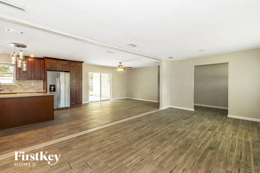 an empty living room with a kitchen and wood flooring
