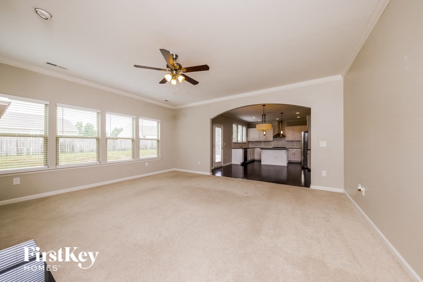 an empty living room with a ceiling fan and a kitchen