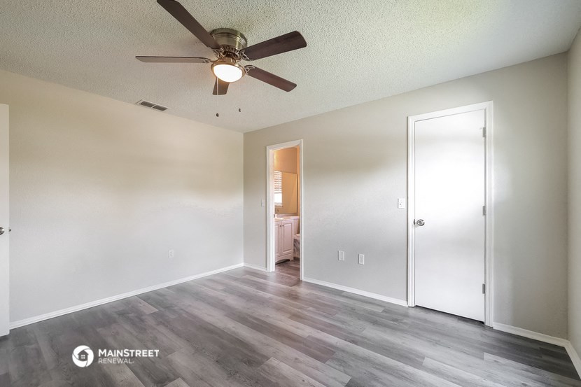 an empty living room with a ceiling fan and a door to a bathroom