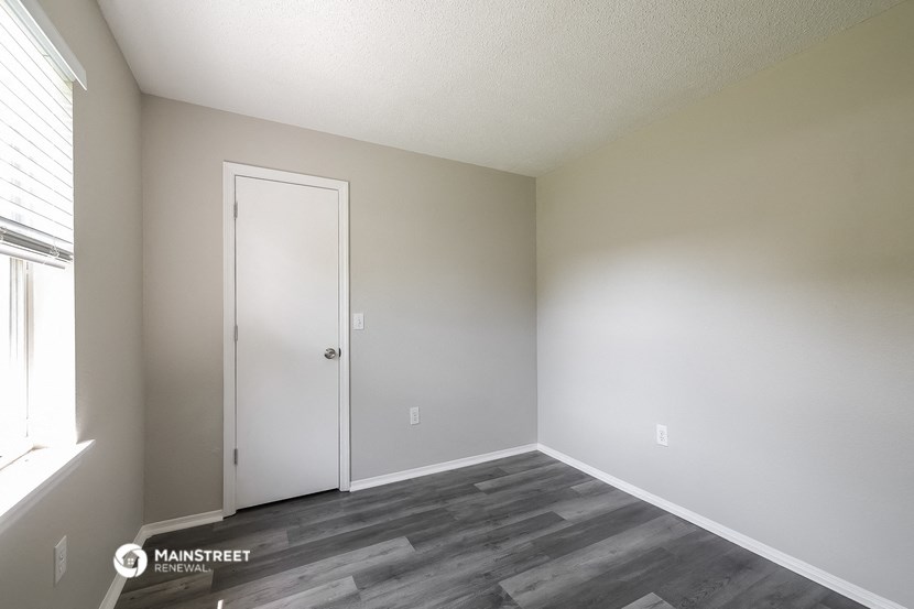 the spacious living room of an apartment with white walls and wood flooring