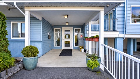 A blue house with a white railing and a black mat in front.