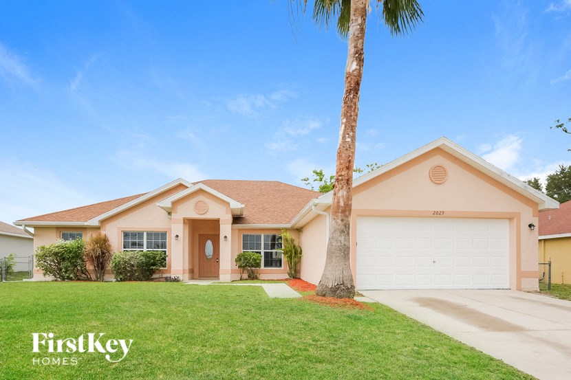 a beige house with a palm tree and a driveway