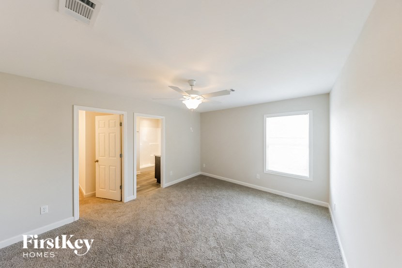 an empty living room with a ceiling fan and a door to a hallway