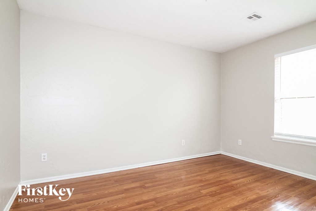 a bedroom with white walls and wood flooring and a window