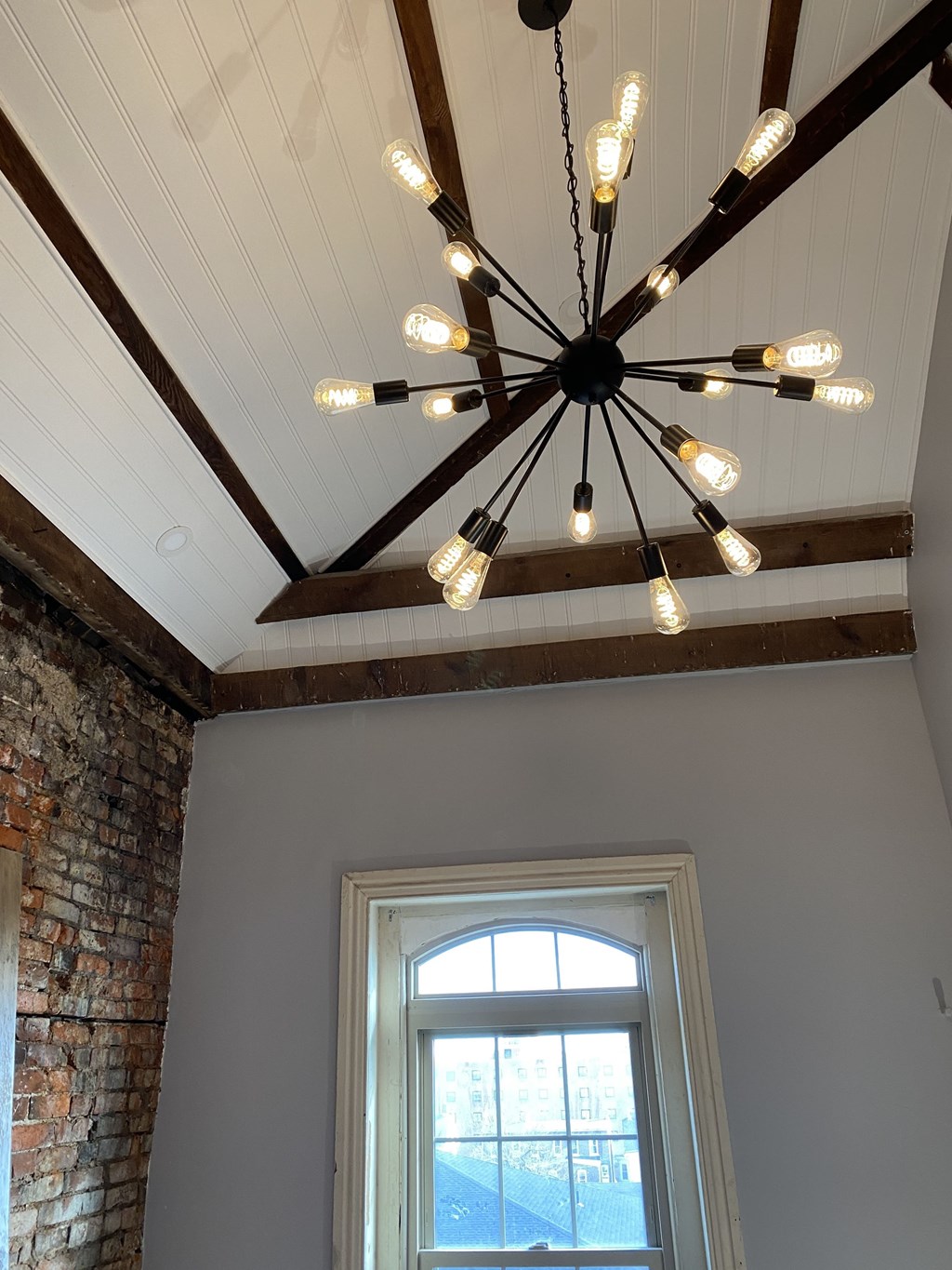 a chandelier in a living room with a window and a brick wall