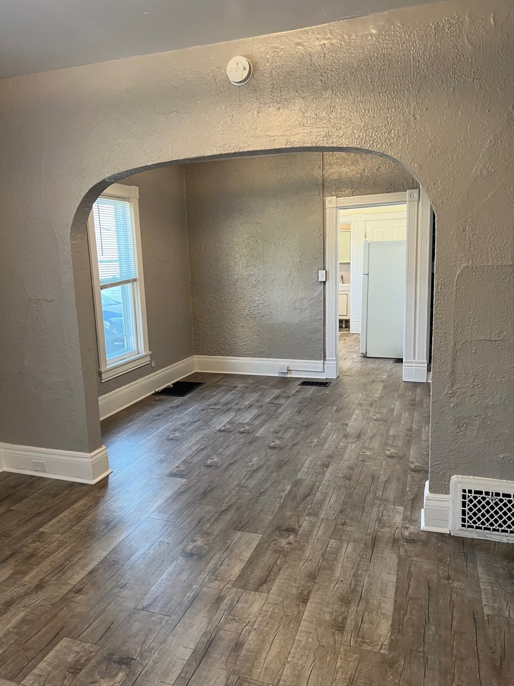 an empty living room with wood flooring and an arched doorway