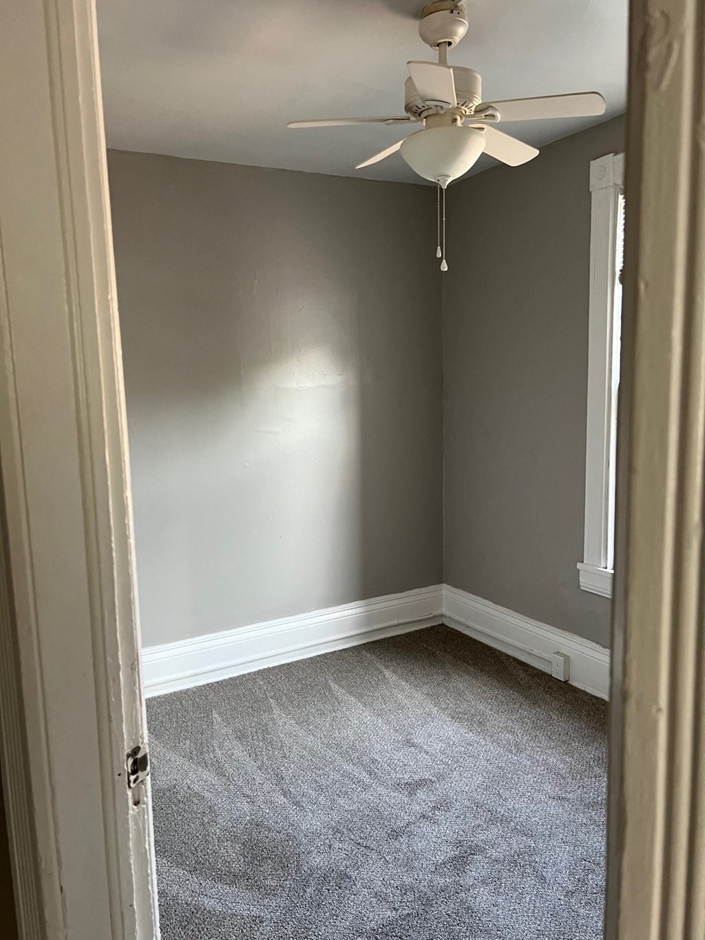 an empty room with a ceiling fan and gray walls