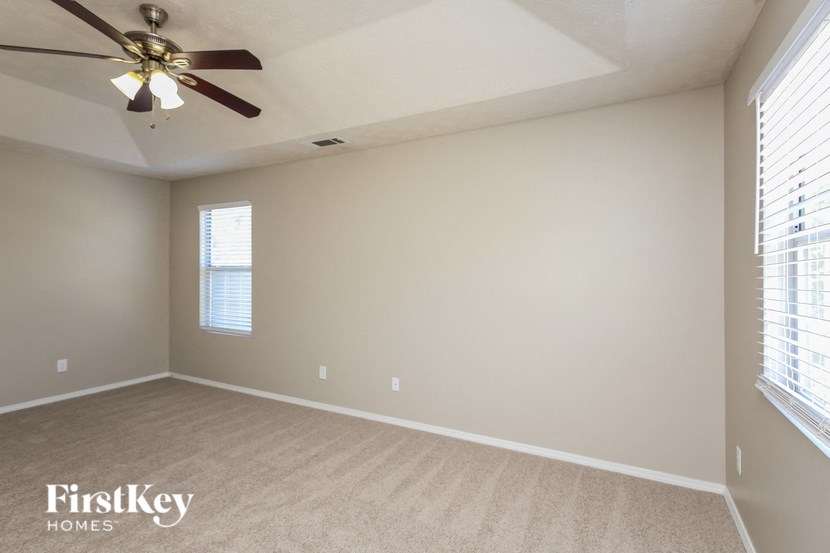 an empty living room with a ceiling fan and two windows