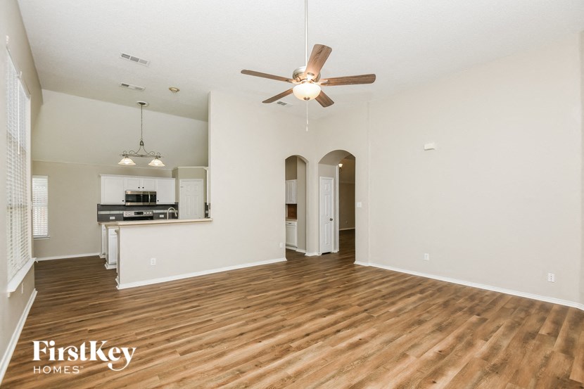 an empty living room with a ceiling fan and a kitchen