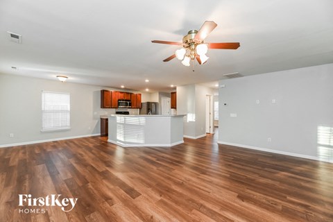 an empty living room with a ceiling fan and a kitchen