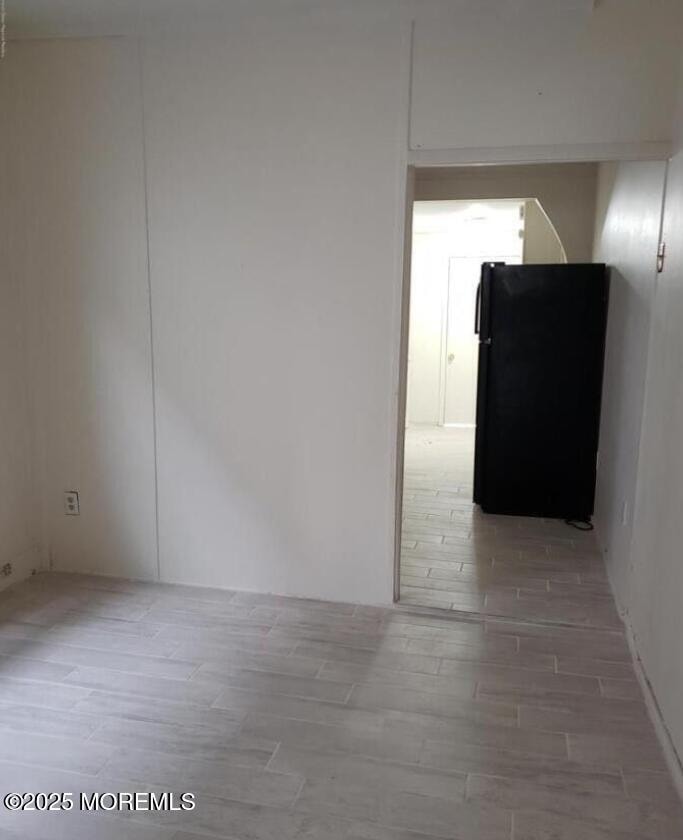 A black refrigerator is in a room with white walls and a tiled floor.