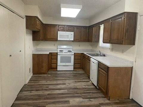 an empty kitchen with wooden floors and white appliances