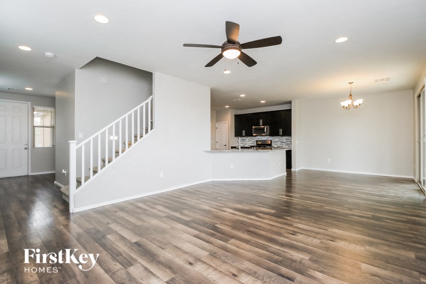 an empty living room with a ceiling fan and a kitchen