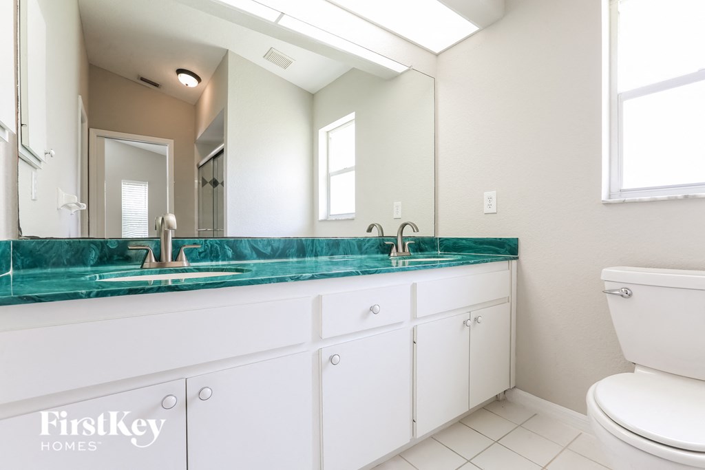 A white bathroom with a green counter top and a toilet.