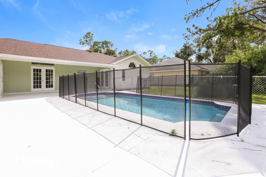 A pool surrounded by a black fence with a house in the background.