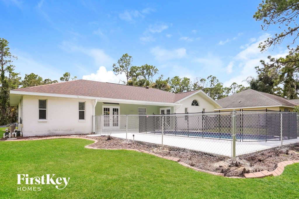 A white house with a brown roof and a fenced in backyard.
