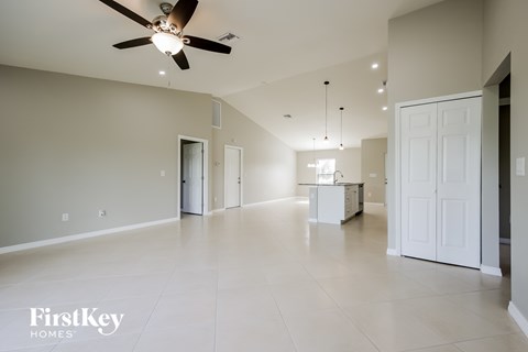 A spacious room with a ceiling fan and a kitchen area in the background.