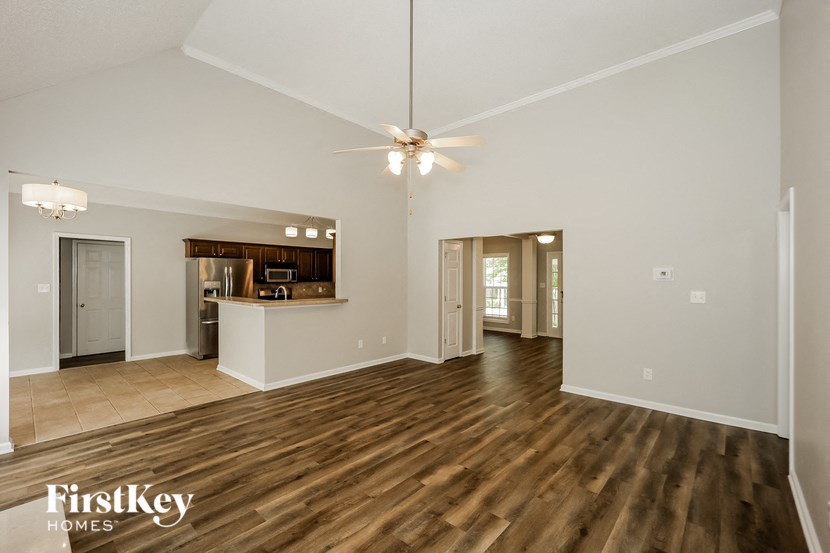 an empty living room with a kitchen and a ceiling fan