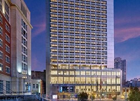 A tall building with many windows is lit up at dusk.